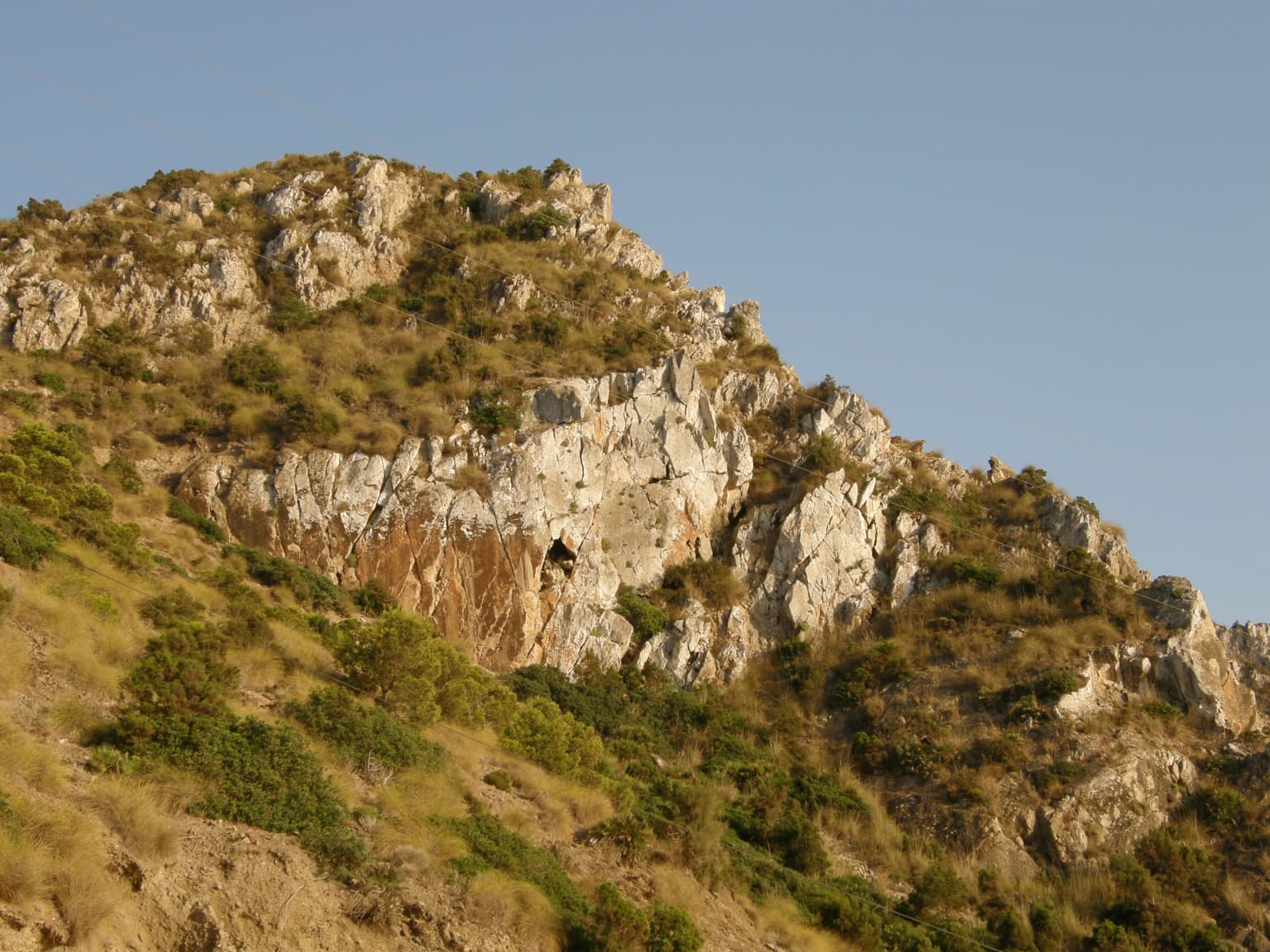Acantilados rocosos de montaña con vegetación escasa bajo un cielo azul claro
