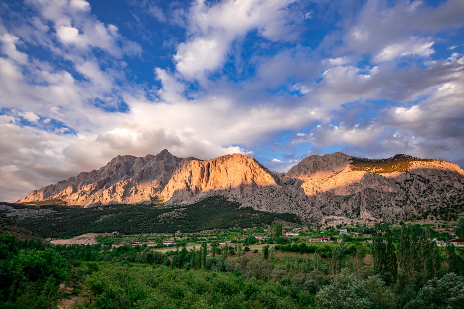Landscape view of Yelatan Village in Aladağlar National Park featuring mountain peaks, green valley, and blue sky with scattered clouds