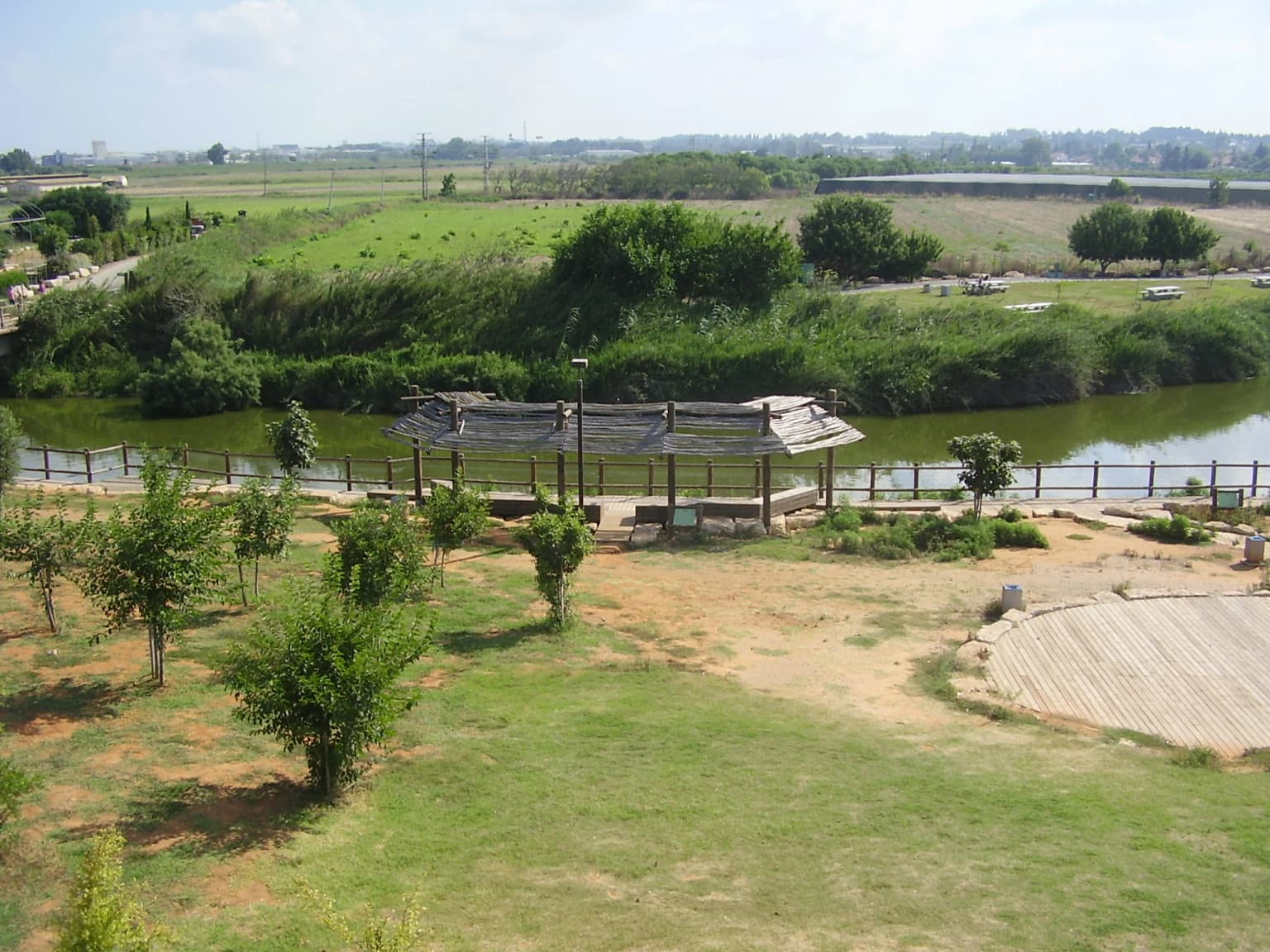 Río con un refugio cubierto y zona de césped, rodeado de árboles y terreno abierto