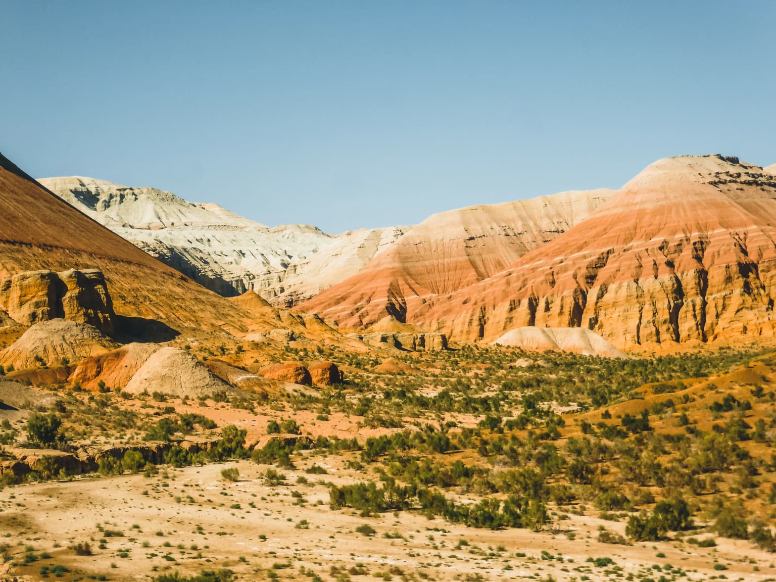 Desert landscape with colorful striped rock formations under clear blue sky