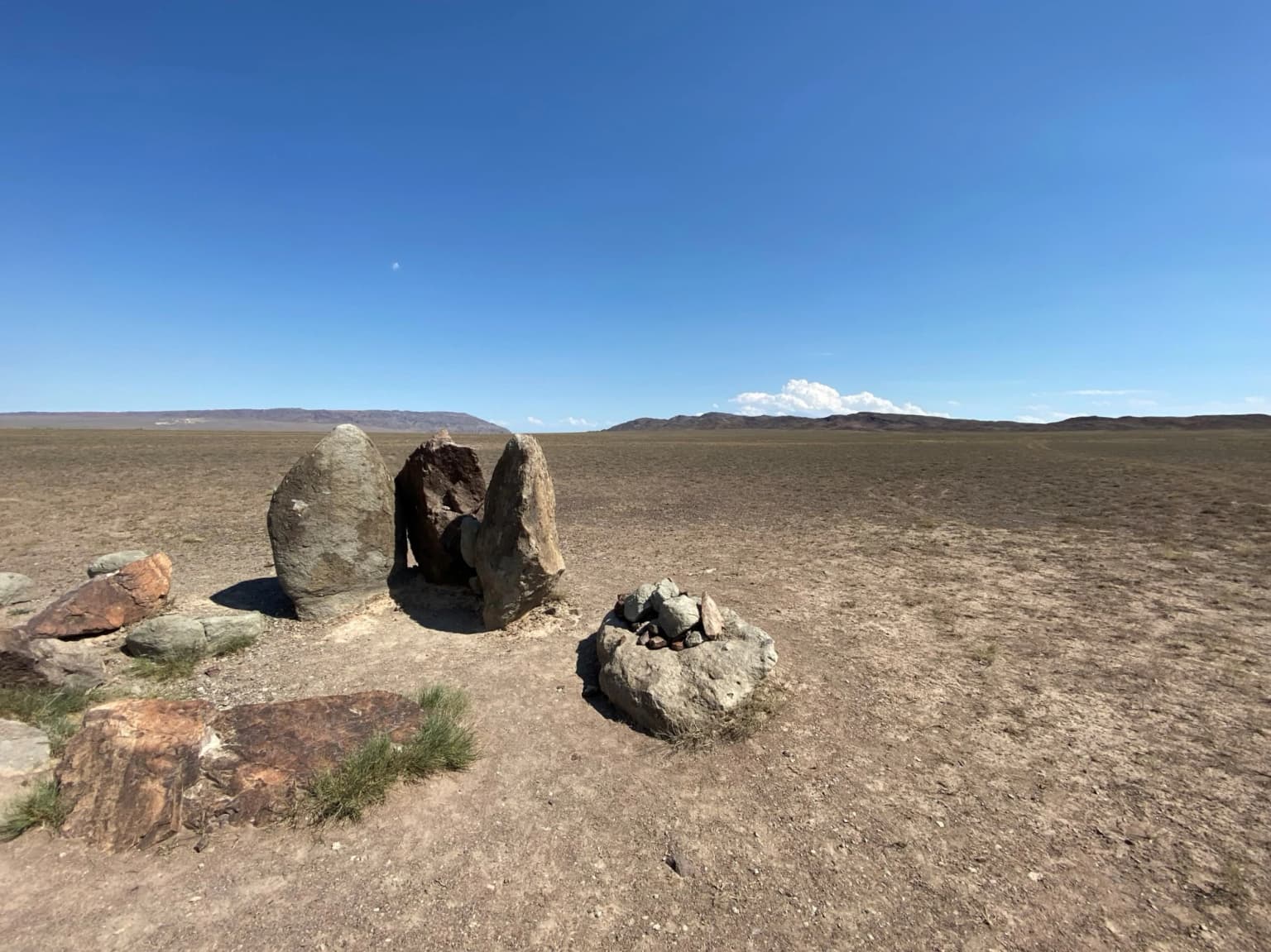 Stone stelae and boulders in a dry, open desert landscape with distant mountains under a clear blue sky