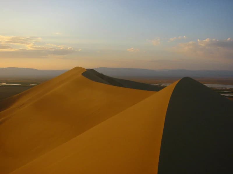 Sand dunes in a desert landscape with mountains in the background