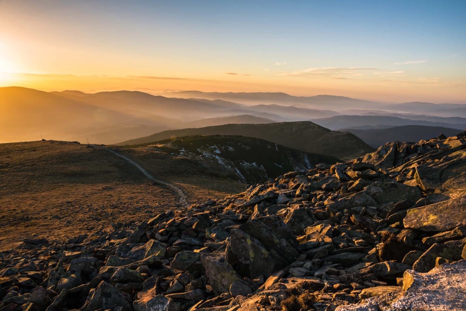 Rocky mountain landscape at sunset with rolling hills and a winding path in the distance