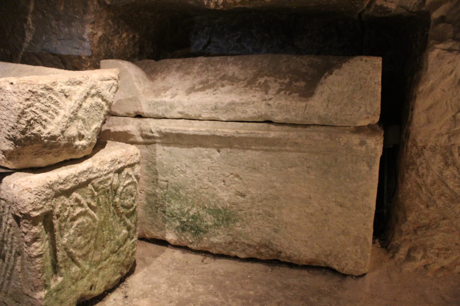 Antiguos sarcófagos de piedra con grabados en el interior de un estrecho pasaje de catacumba