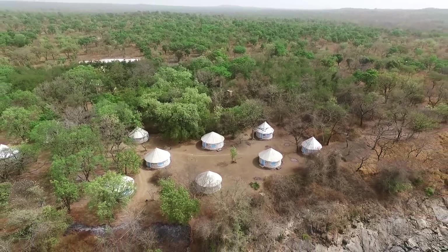 Vista aérea de un paisaje de sabana con chozas redondas dispersas, árboles escasos y terreno seco