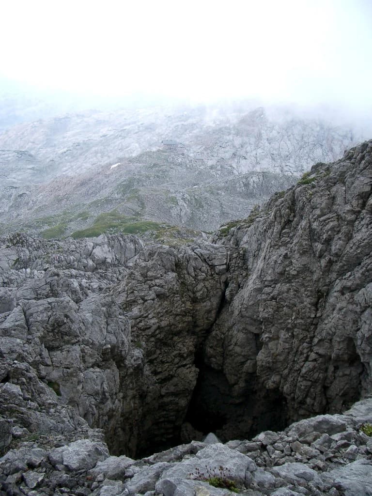Rocky cave entrance in mountainous terrain with misty background and rocky cliffs