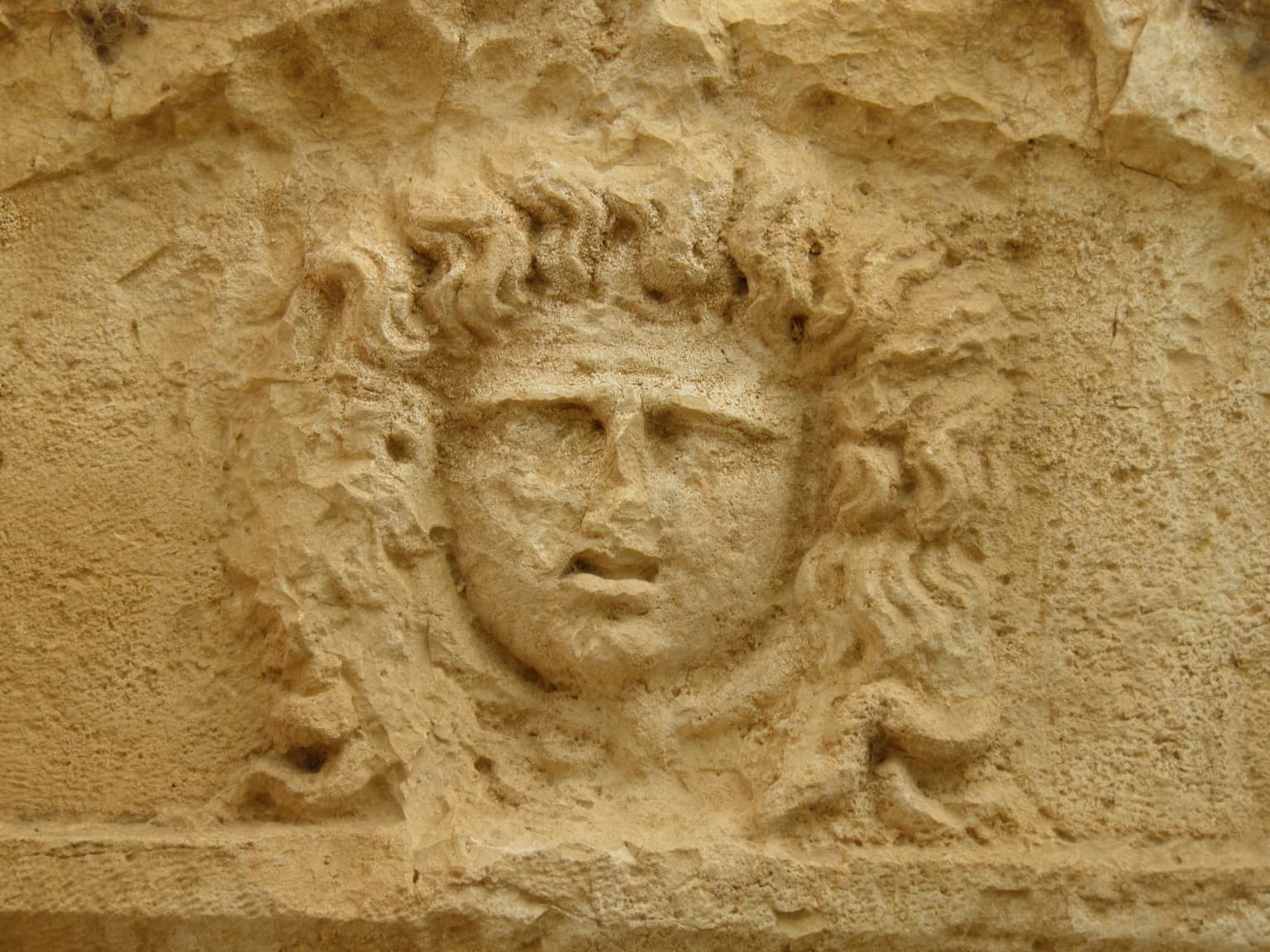 Stone relief sculpture of a human face with curly hair on a weathered stone surface