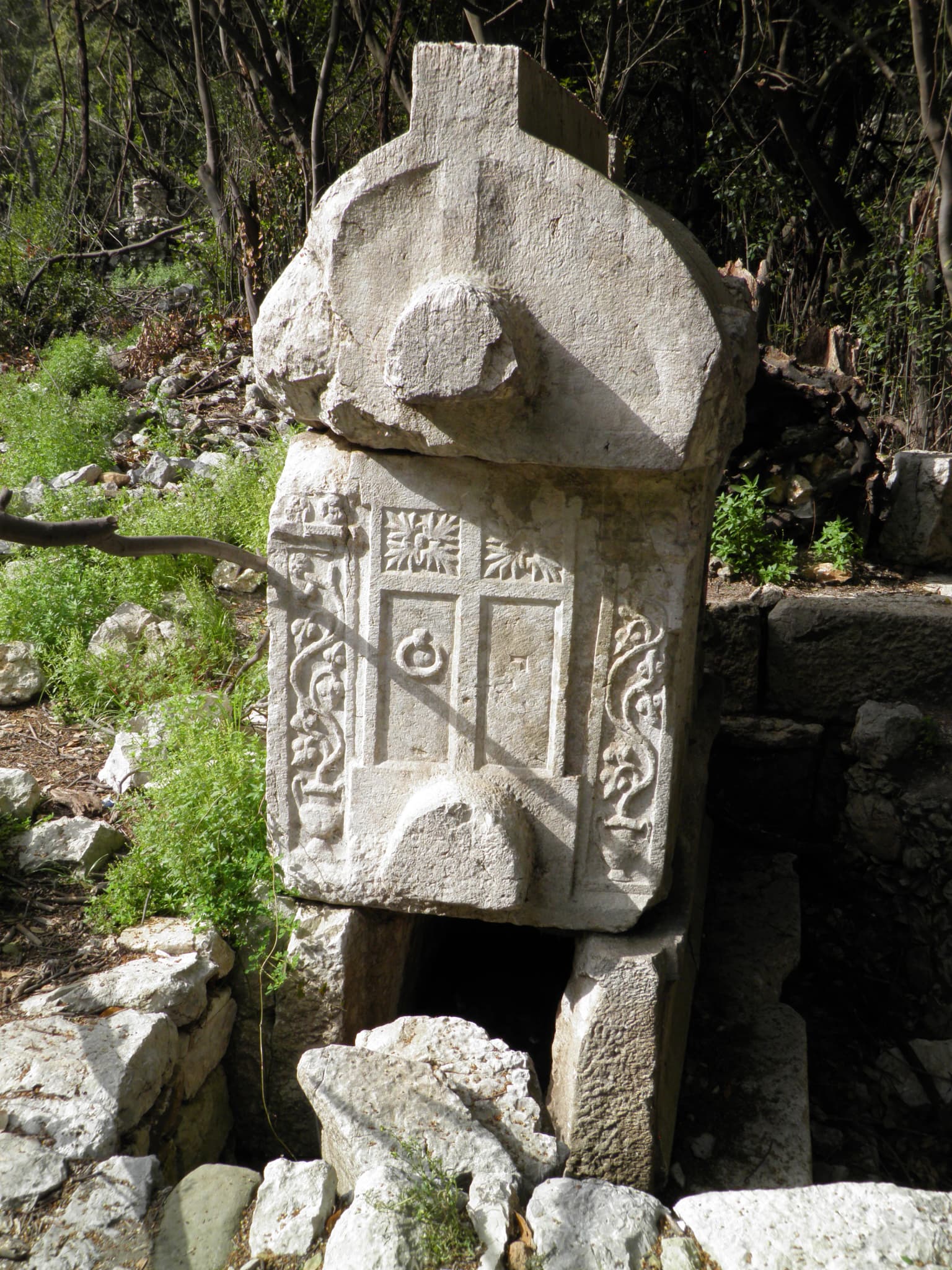 Stone monument with intricate carvings surrounded by rocks and greenery