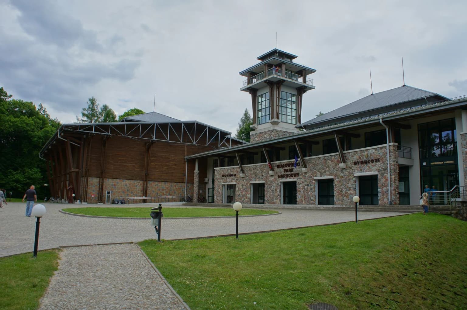 Stone visitor center building with observation tower, paved courtyard, and green lawn in Białowieża National Park
