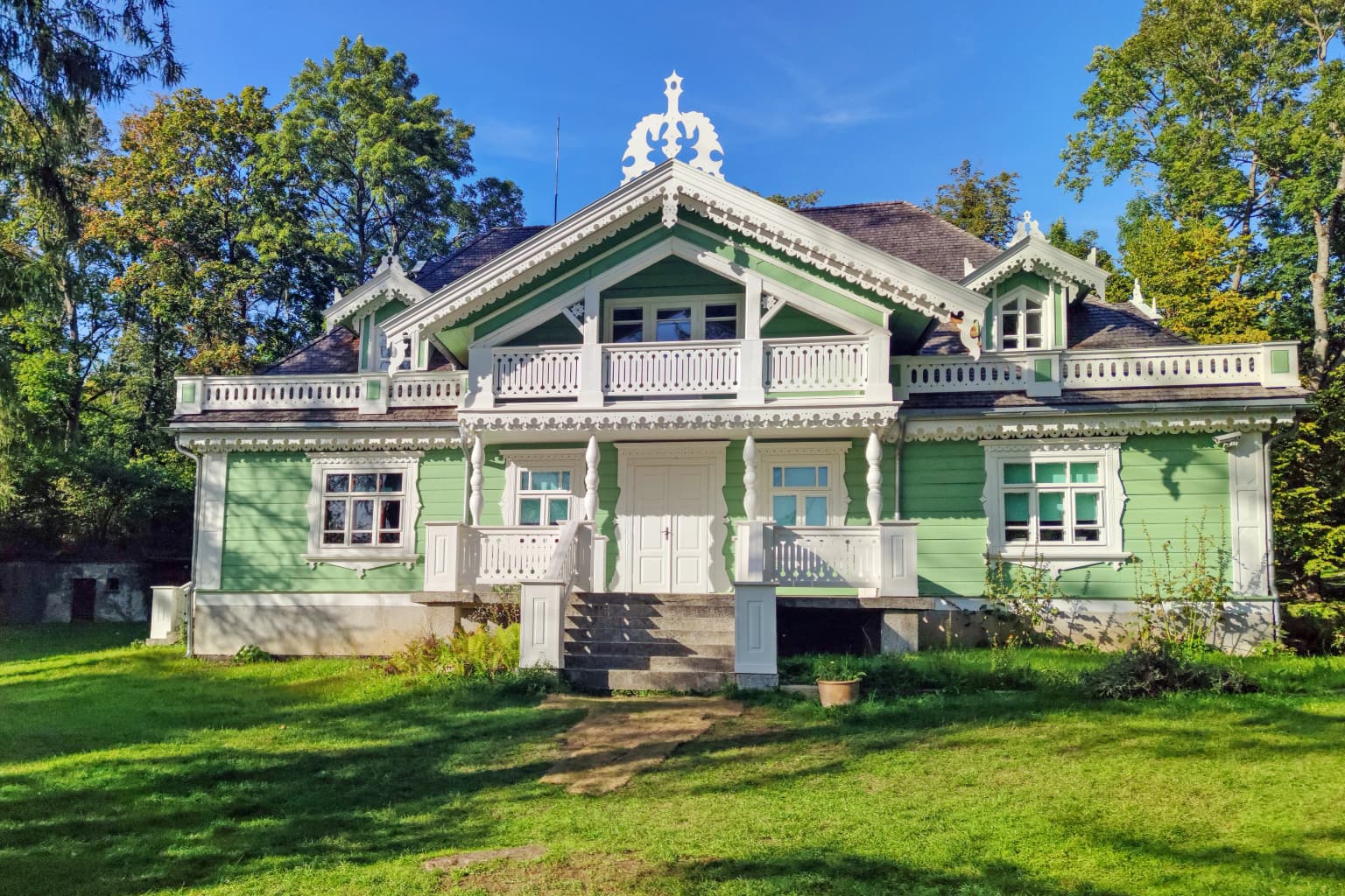 Green two-story hunting lodge with white trim and central tower, surrounded by grassy area and trees