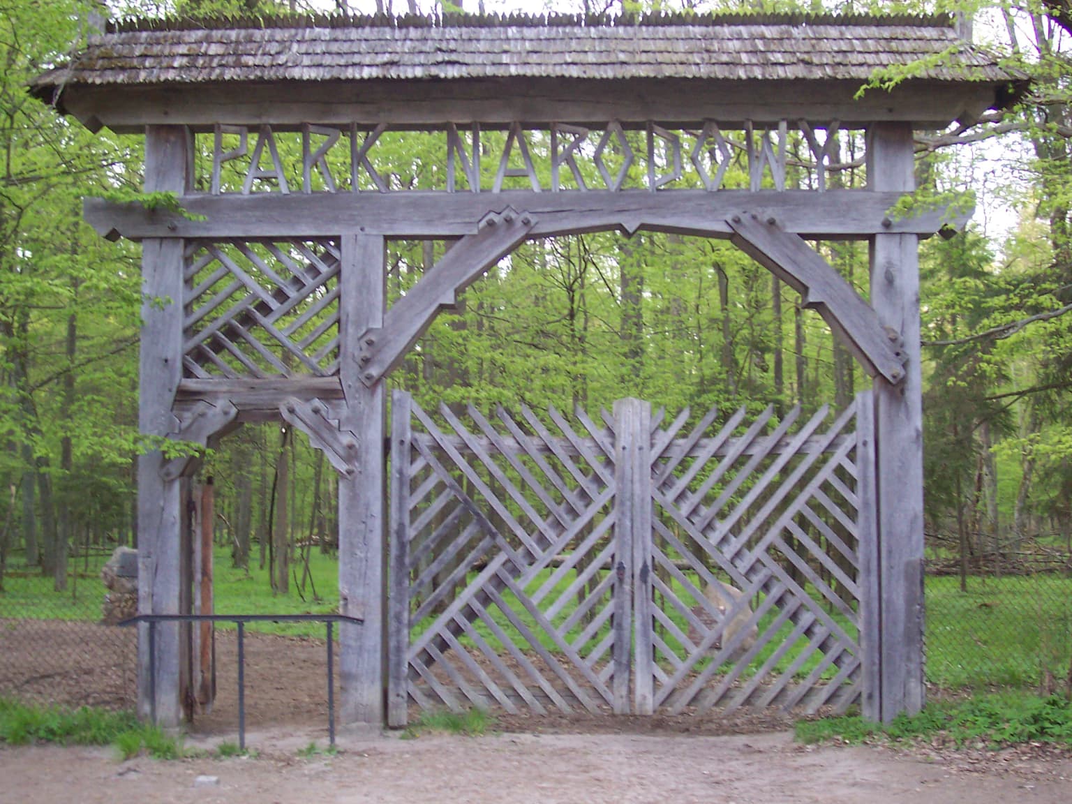 Wooden gate structure with lattice design and 'PARK NARODOWY' lettering at the entrance to a forested area