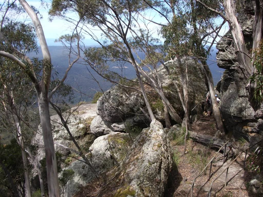 Rocky outcrops, eucalyptus trees, and distant mountain ranges visible from a high elevation viewpoint