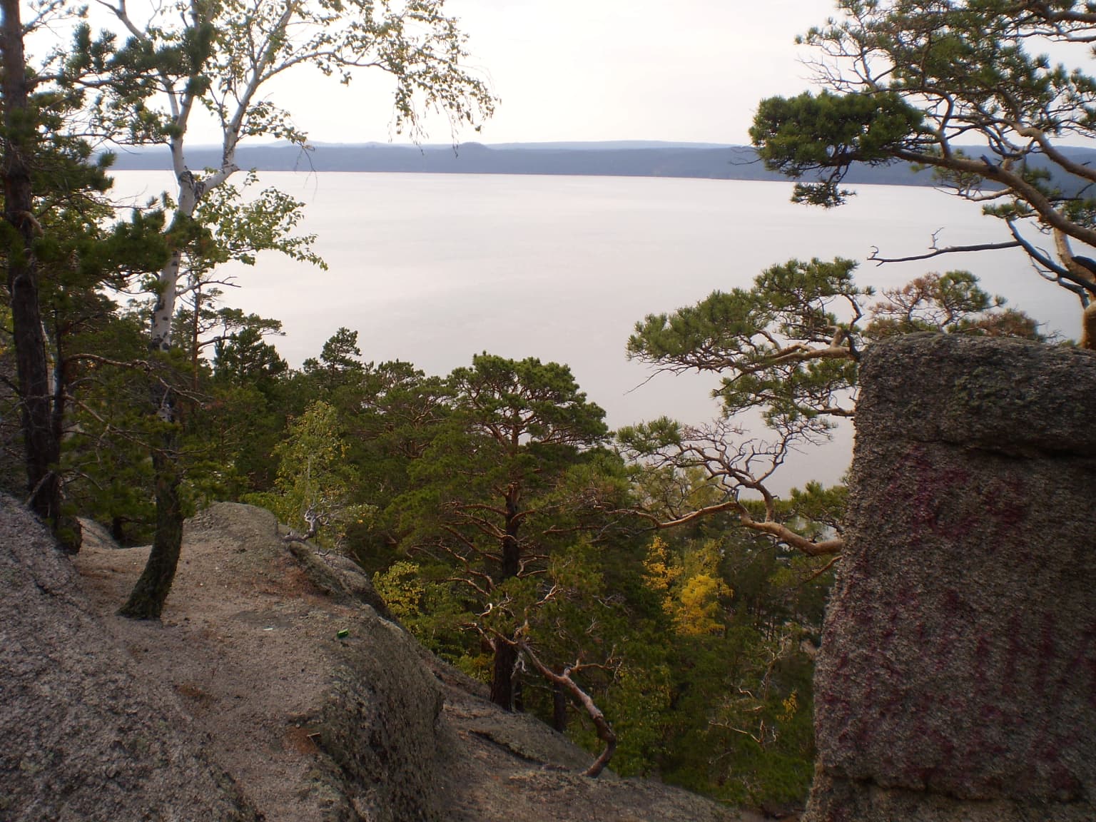 A lake surrounded by forested hills and rocky terrain under an overcast sky