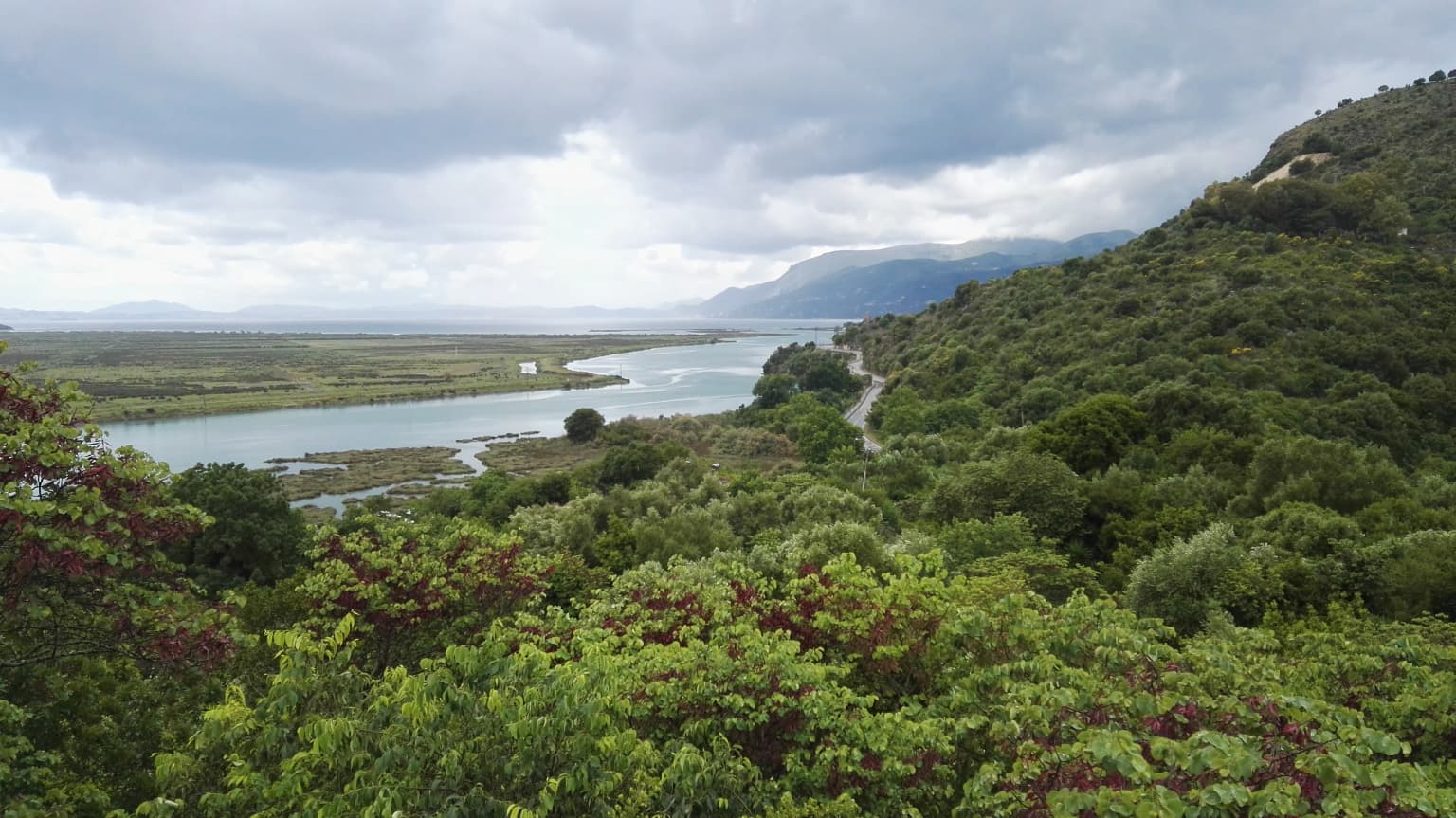 Wide landscape view of the Vivari Channel surrounded by dense green vegetation and rolling hills under an overcast sky