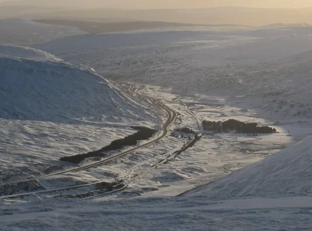 Wide view of snow-covered mountain pass with winding road through valley between hills