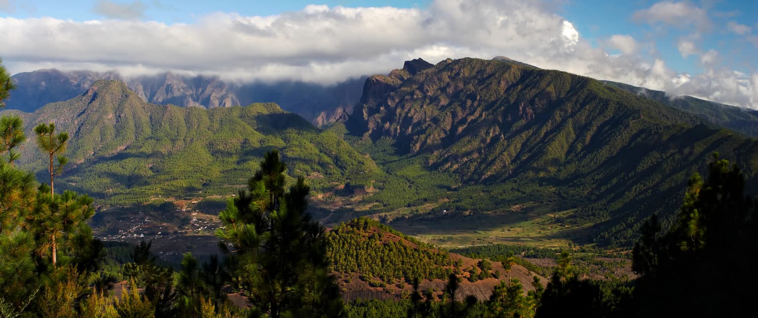 Panoramic view of Caldera de Taburiente National Park featuring mountainous landscape, green valleys, and scattered trees under a partly cloudy sky