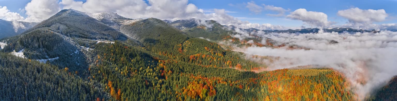 Panoramic landscape of Carpathian National Nature Park with mountain peaks, autumn-colored forests, and low-lying clouds