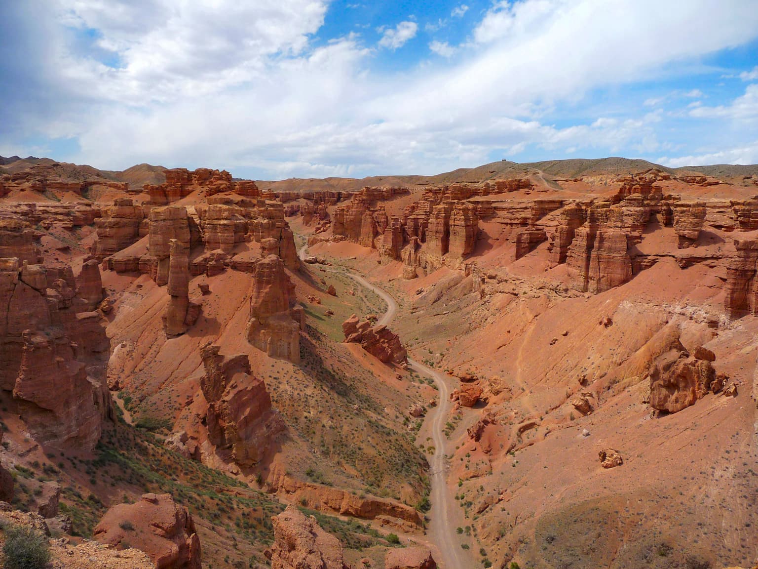 Red rock canyon landscape with winding road, sparse vegetation, and blue sky with clouds