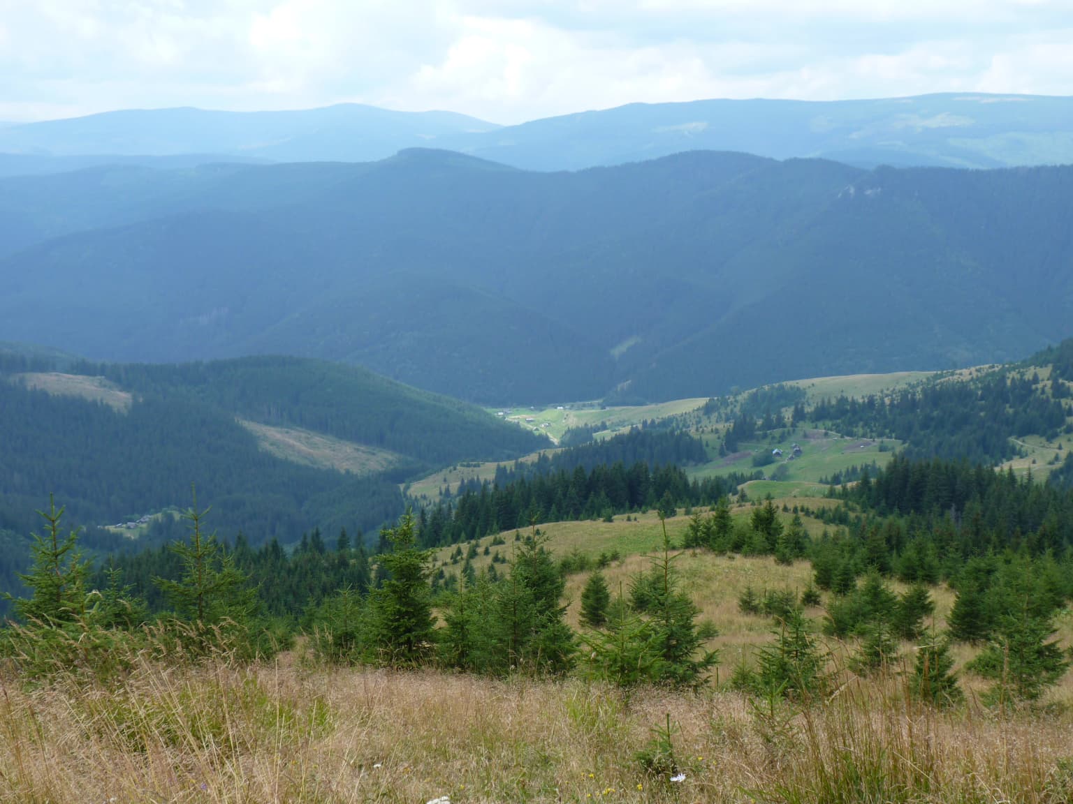 Wide view of mountain ridges, valleys, and forested slopes under a partly cloudy sky