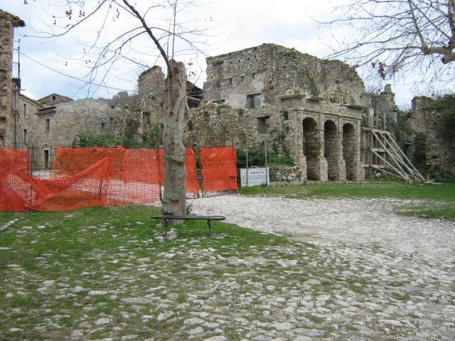 Stone ruins with orange construction netting, a tree, and cobblestone path in grassy area