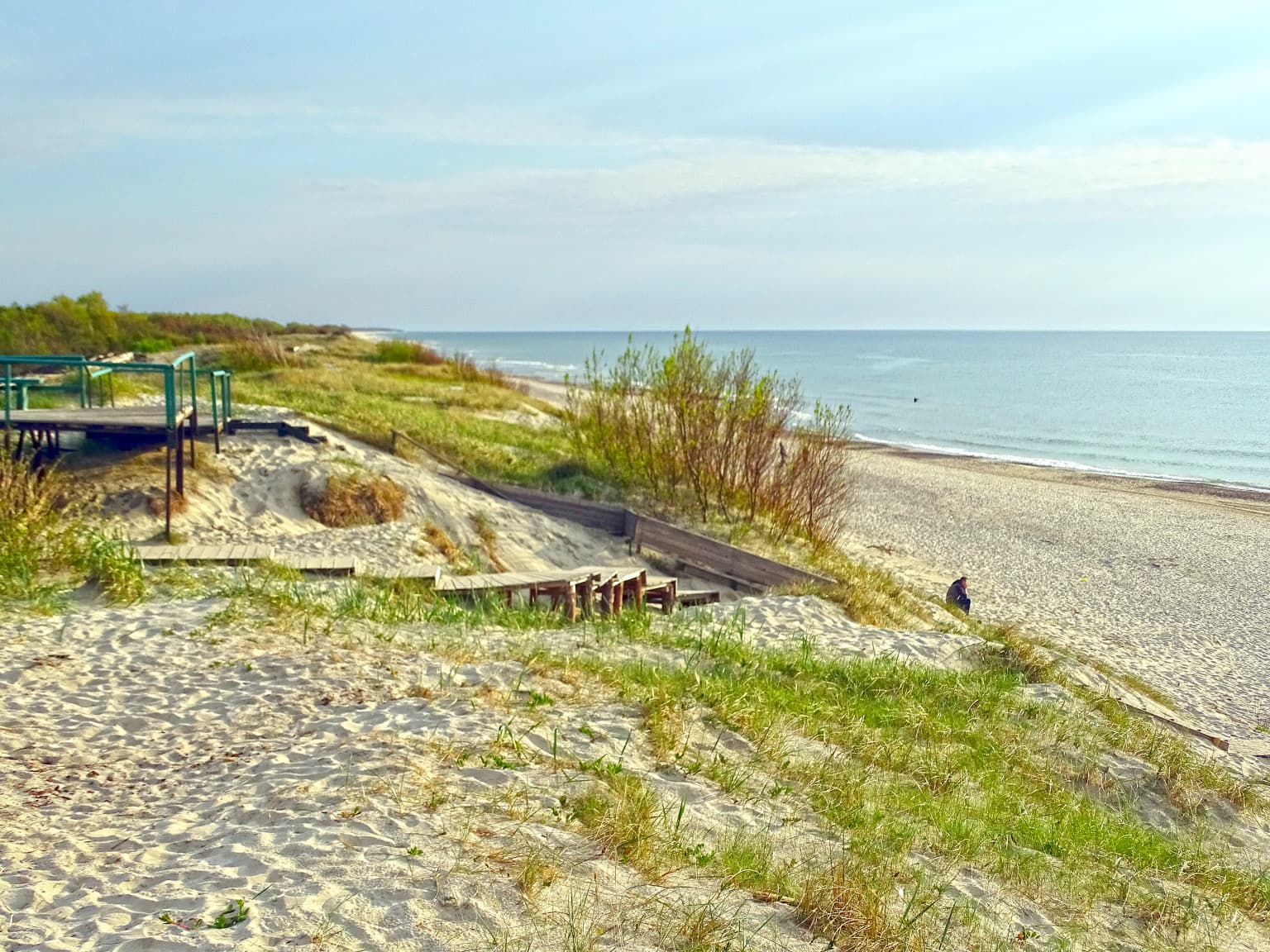 Sandy beach with grassy dunes, wooden boardwalk, and the Baltic Sea in the background