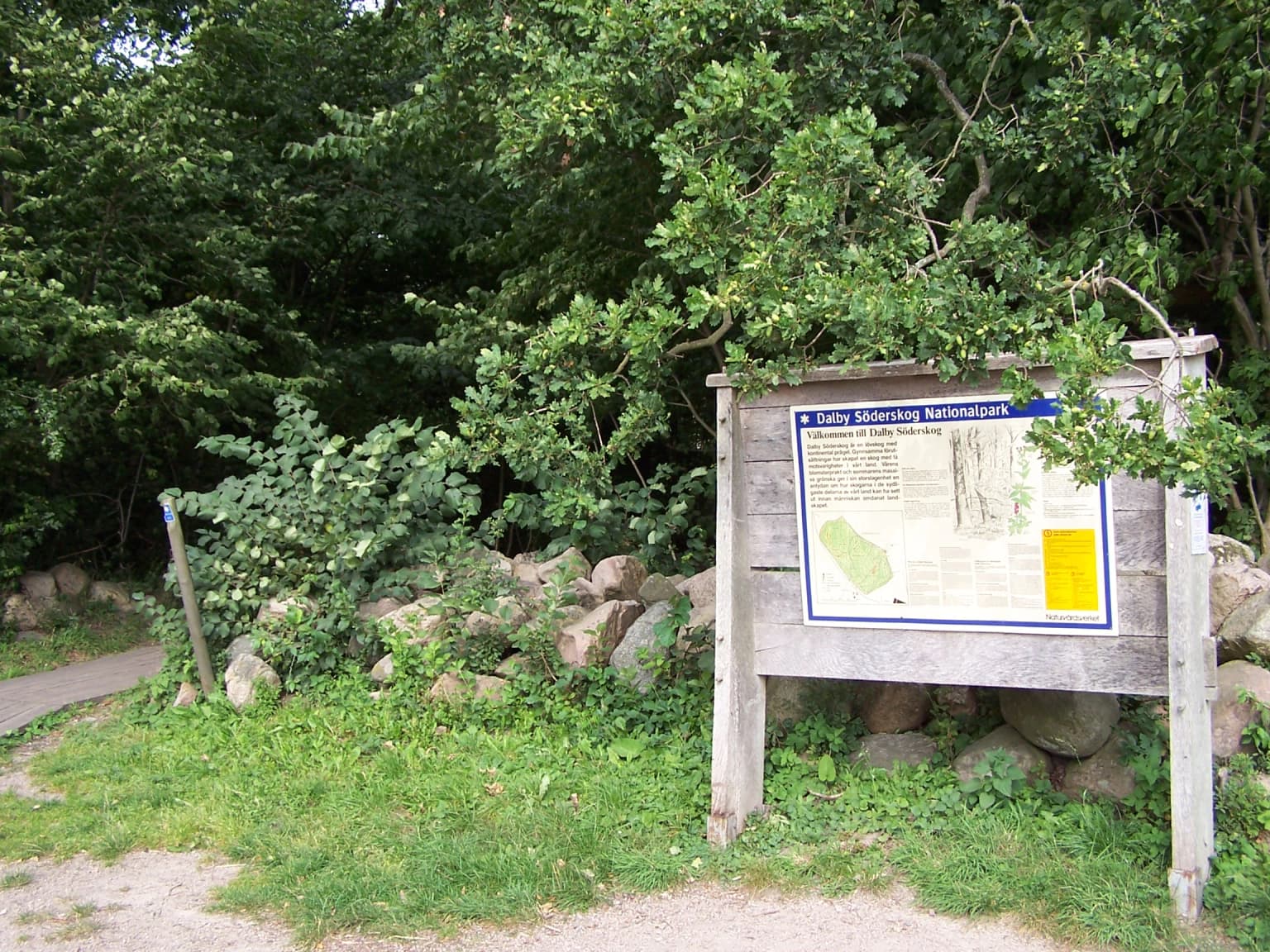 Wooden information sign for Dalby Söderskog National Park mounted on posts with trees and rocks in background