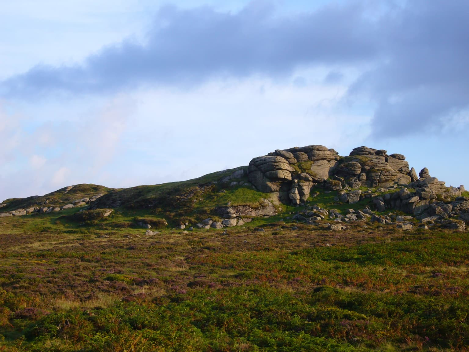 Rocky tor formations on moorland under a partly cloudy sky with scattered vegetation