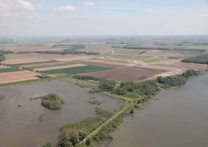 Aerial view showing wetland areas with water channels, adjacent agricultural fields, and a river in the distance