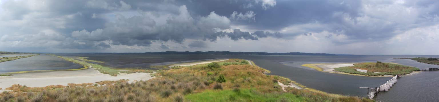 Panoramic view of Karavasta Lagoon with coastal marshland, distant hills, and cloudy sky.
