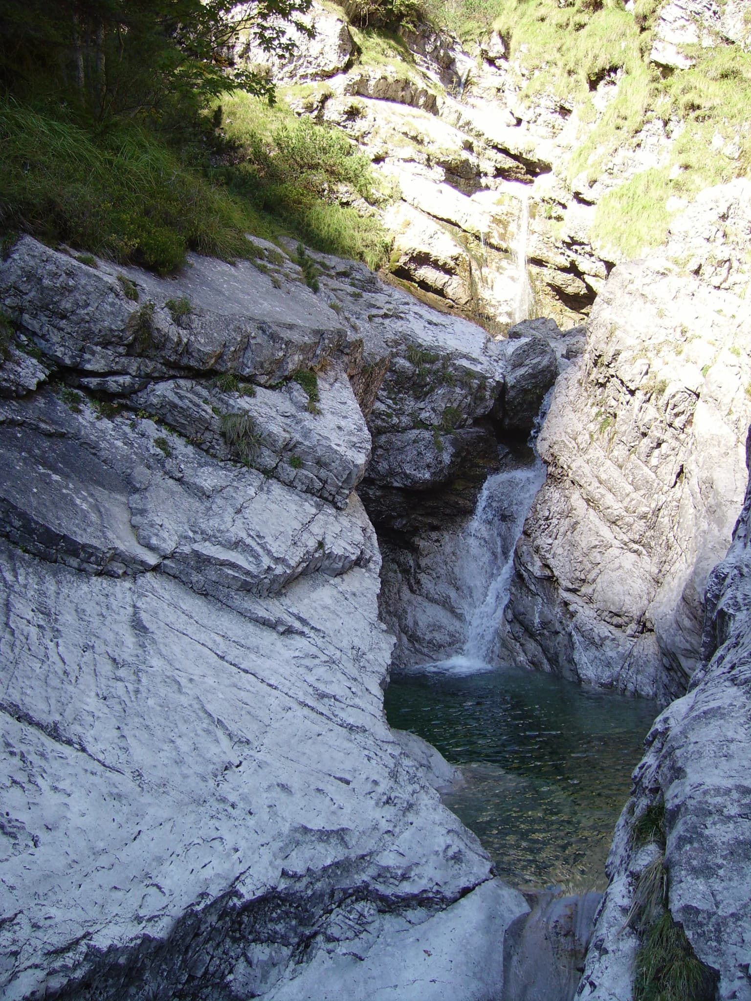 A small waterfall cascading into a rocky pool surrounded by green vegetation and stone cliffs