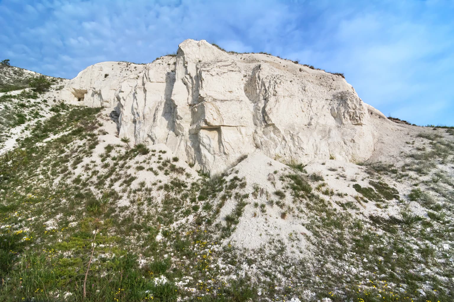 White chalk cliffs with sparse green vegetation on a hillside under a partly cloudy blue sky