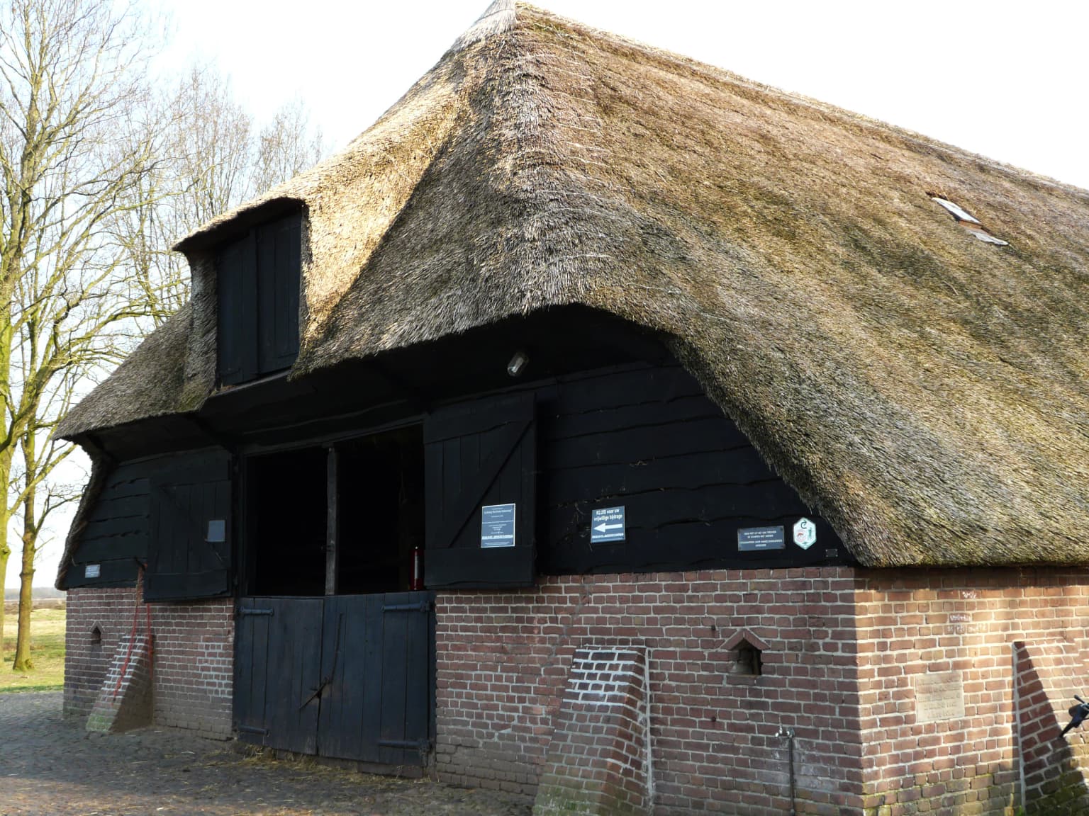 Traditional brick building with thatched roof and black wooden doors, featuring informational plaques on the exterior