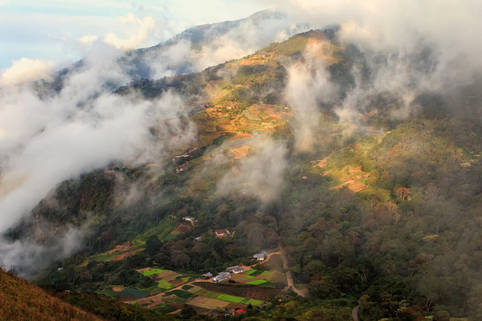 Mountainous landscape with clouds, valleys, and scattered buildings below