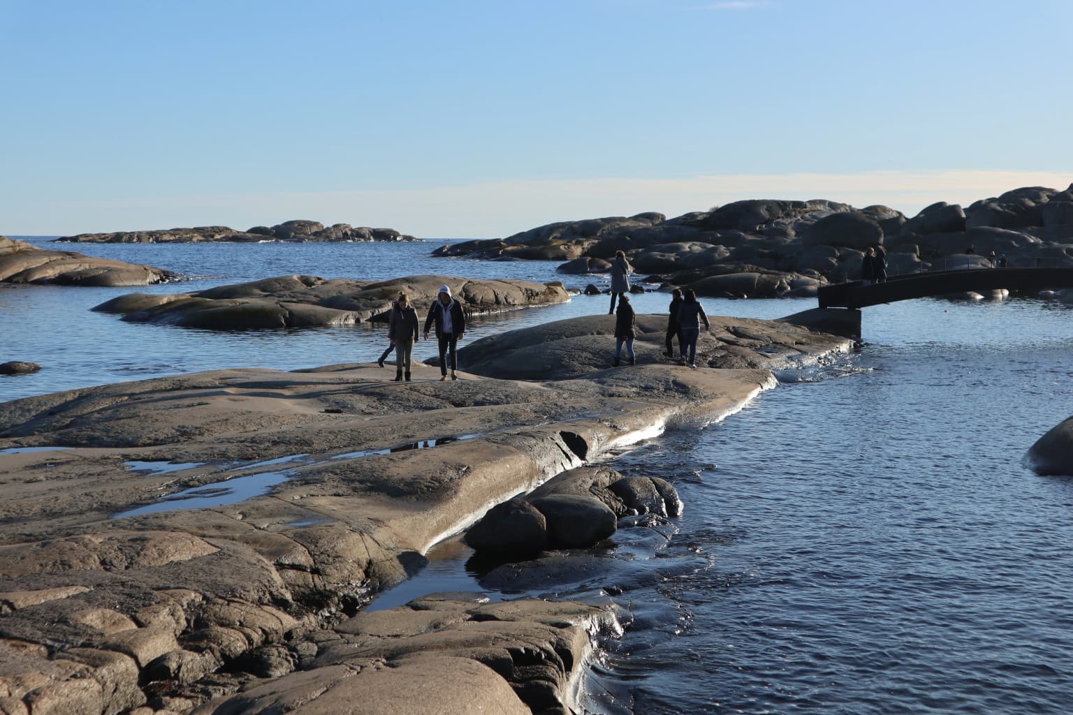 Rocky coastal shoreline with people walking on flat rocks near the water in Færder National Park