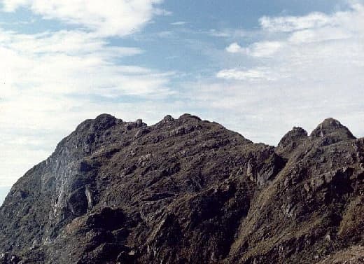Picos montañosos de Punta Pance bajo un cielo parcialmente nublado con terreno escarpado visible y nubes distantes