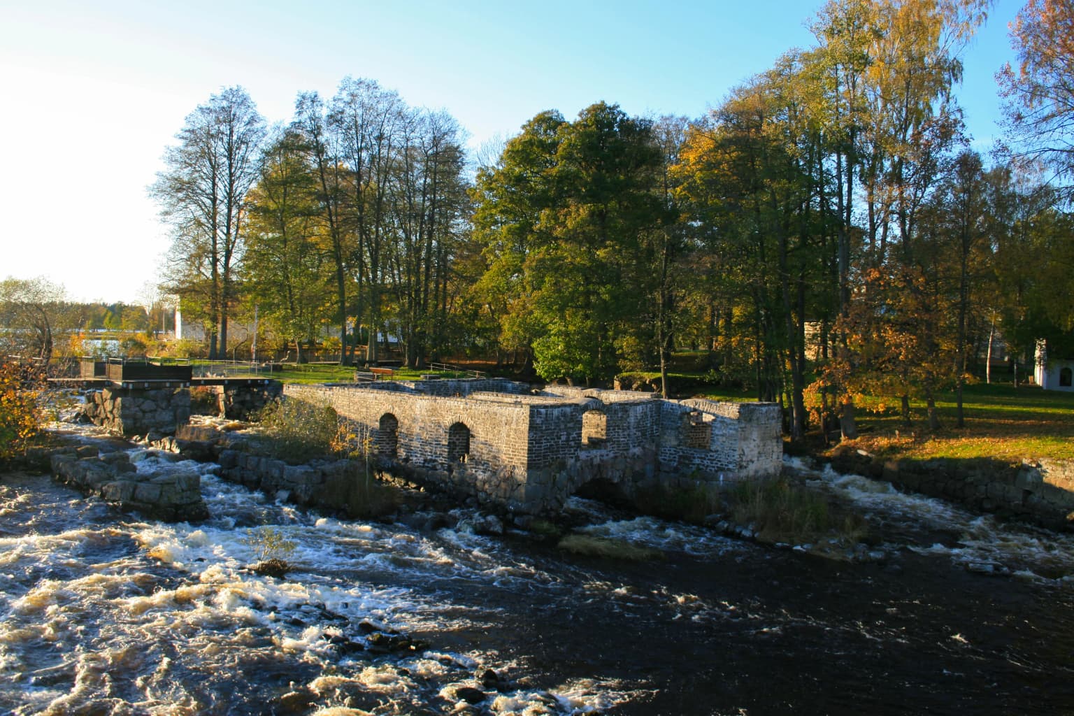 Stone structure of old mill on river with flowing water and trees in background