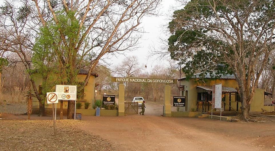 Dirt road leading to yellow building entrance with 'PARQUE NACIONAL DA GORONGOSA' sign and parked vehicle