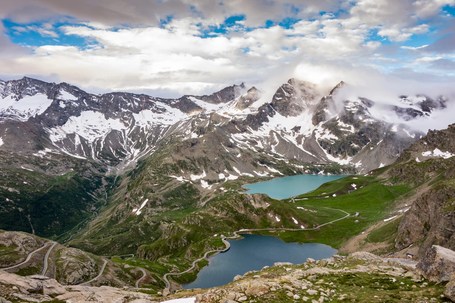 Panoramic view of snow-capped mountains, blue alpine lakes, and winding trails in a mountainous national park.