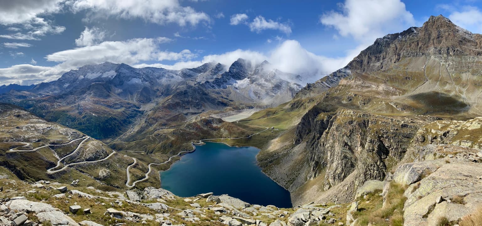 Panoramic landscape view from Colle del Nivolet showing Lago Serrù and Lago dell'Agnel surrounded by mountain peaks under a partly cloudy sky
