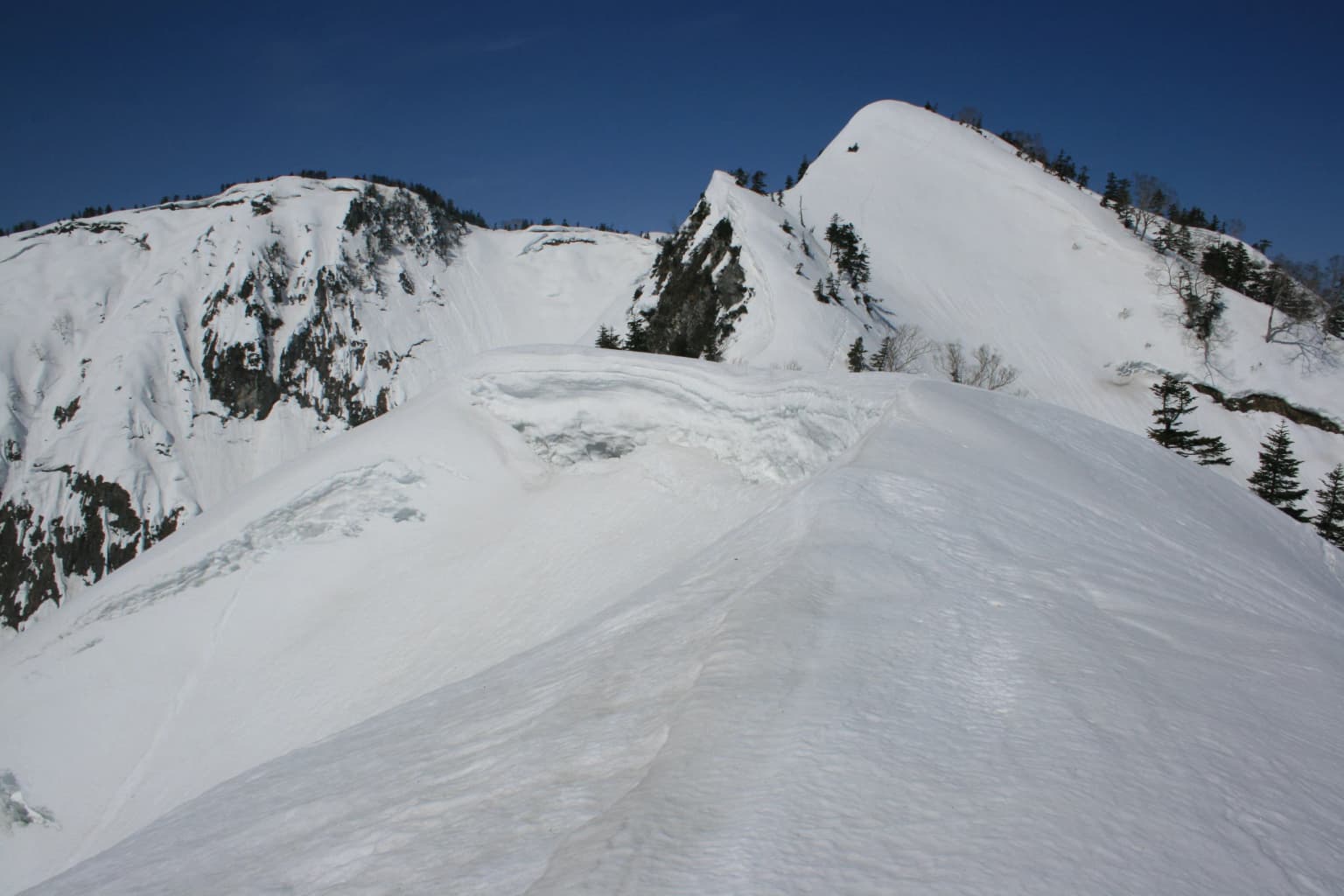 Cordillera montañosa cubierta de nieve con formación de cornisa bajo un cielo azul despejado