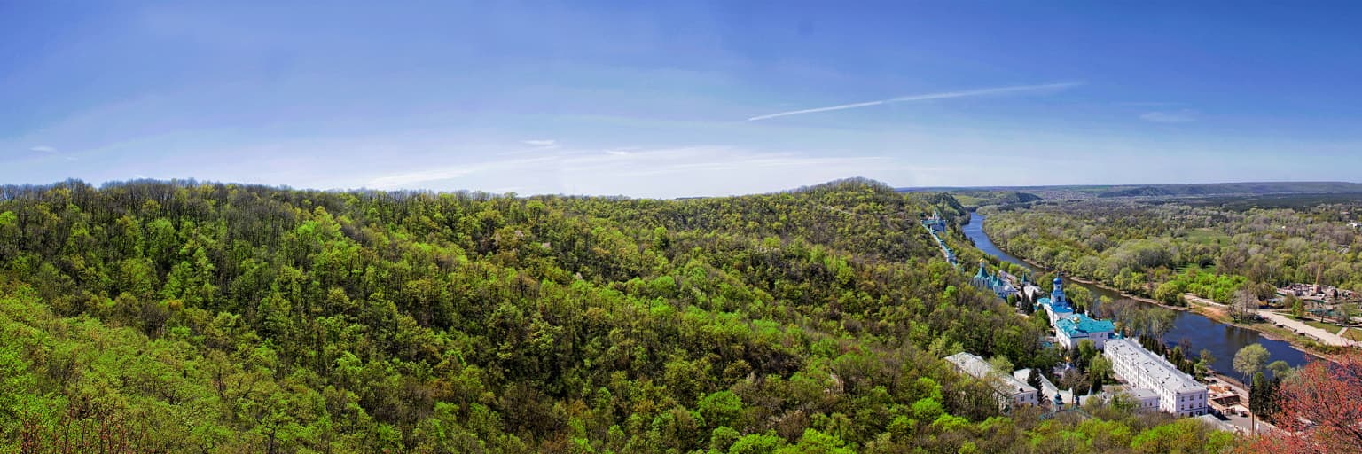Panoramic landscape of Holy Mountains National Nature Park with dense green forests, a winding river, and distant hills under a clear blue sky