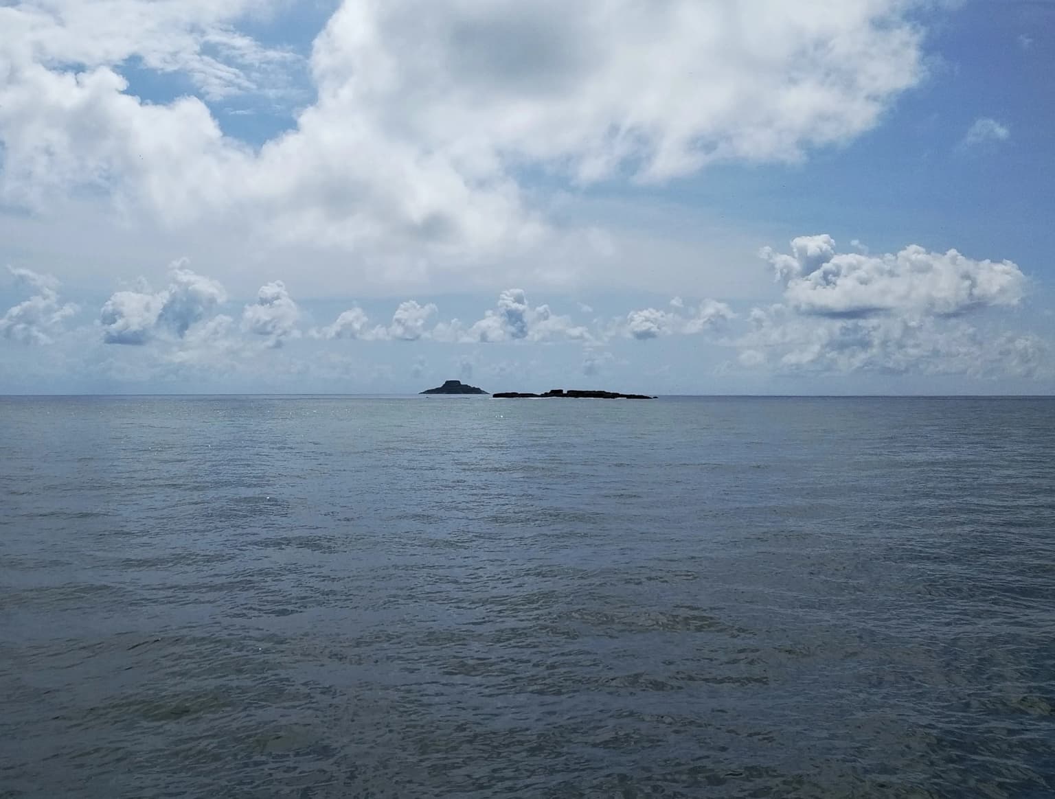 Calm ocean with two small islands on the horizon under a partly cloudy sky