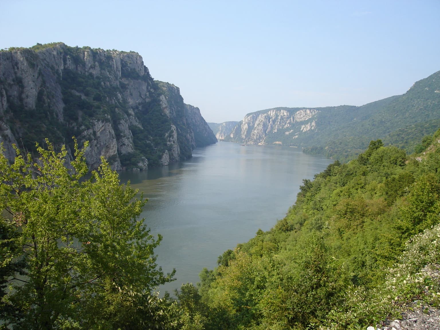 Wide river flanked by rocky cliffs and green vegetation under a clear blue sky.