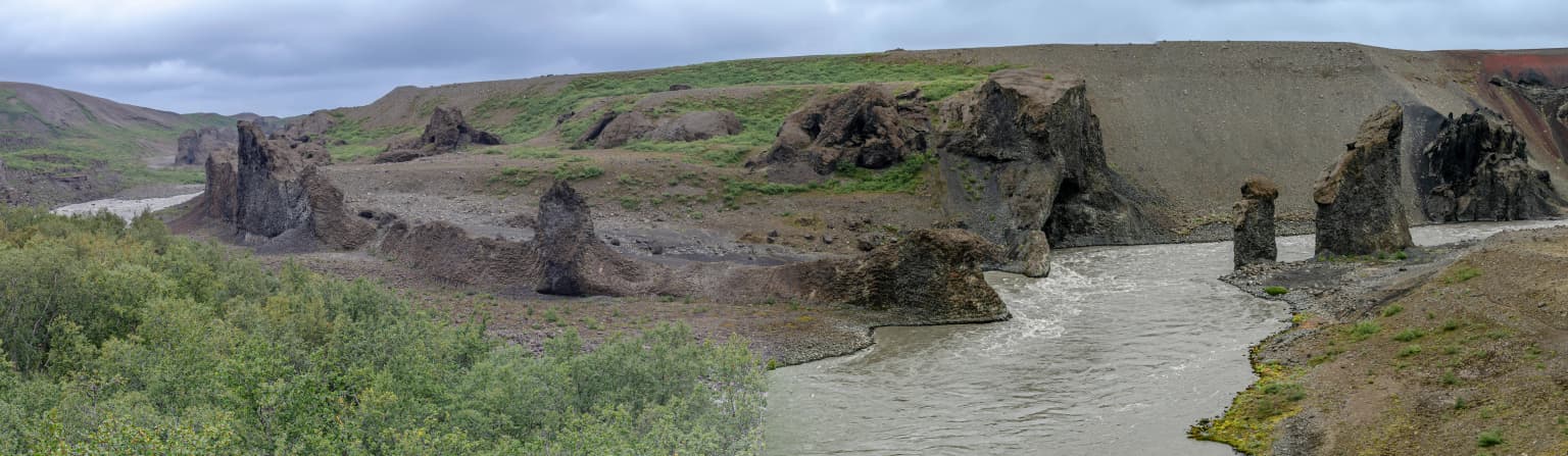 River flowing through a canyon with distinctive rock formations and green vegetation under a cloudy sky