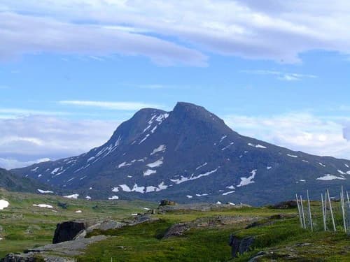 Mountain summit with patches of snow, grassy terrain, and a clear blue sky