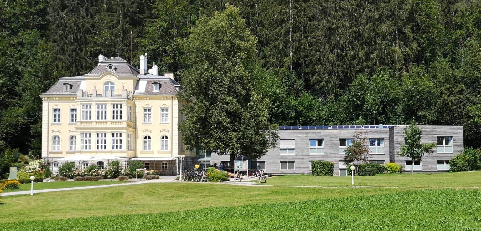 Historic yellow building with white trim and gray roof surrounded by green fields and trees
