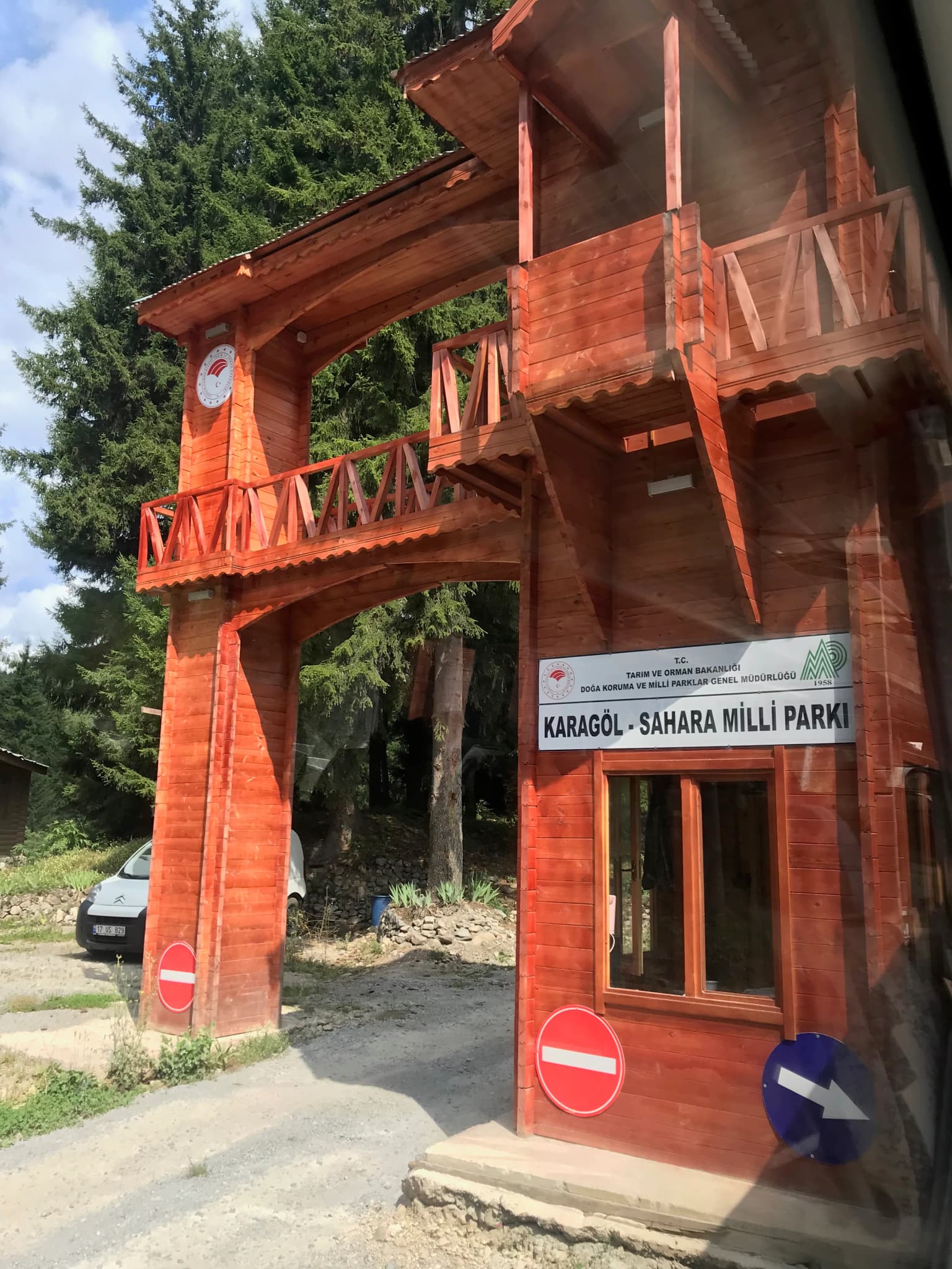 Wooden archway entrance to Karagöl-Sahara National Park with sign reading KARAGÖL - SAHARA MILLİ PARKI, traffic signs, and forest background