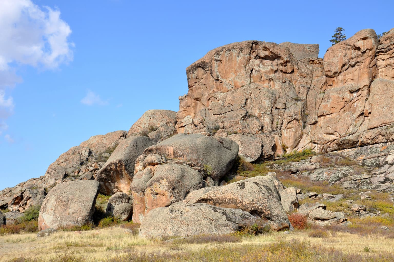 Large rock formations and boulders on a grassy plain with a clear blue sky