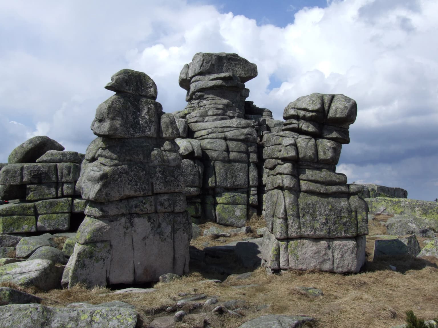 Stacked rock formations with moss-covered surfaces on a mountain ridge under a partly cloudy sky