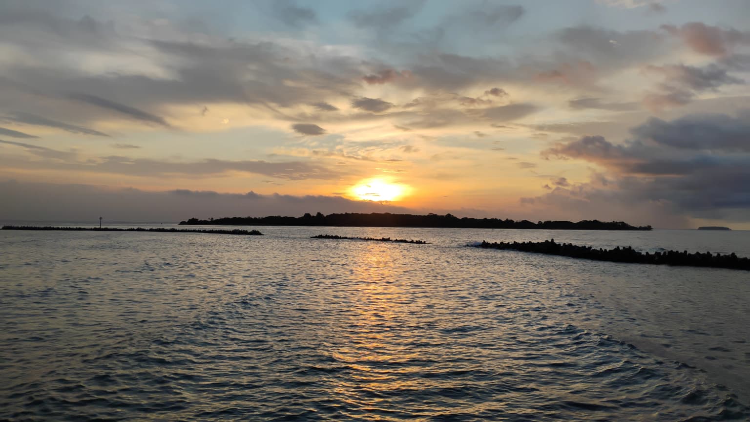 Sunset over a body of water with a distant island chain under a partly cloudy sky